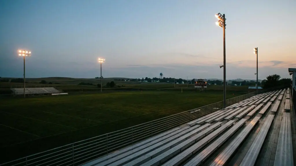 Nebraska high school football stadium at dusk, stadium lights turning on