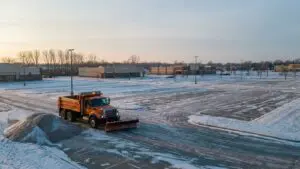 Snowplow truck idling beside a salt pile at a snow-dusted Omaha commercial plaza at sunrise
