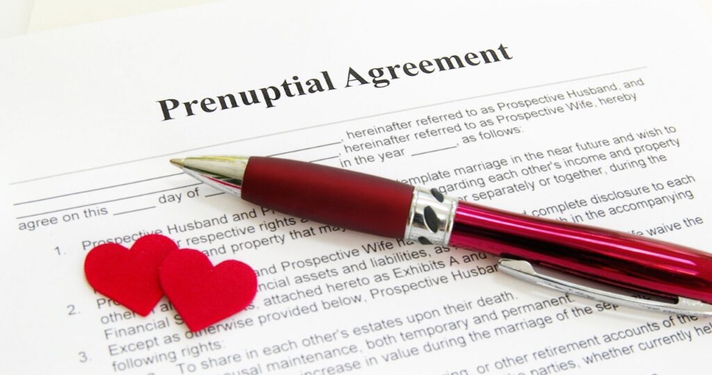 A document titled 'Prenuptial Agreement' resting on a table with a red pen and two small red hearts, symbolizing legal preparation for marriage.