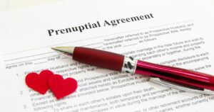 A document titled 'Prenuptial Agreement' resting on a table with a red pen and two small red hearts, symbolizing legal preparation for marriage.